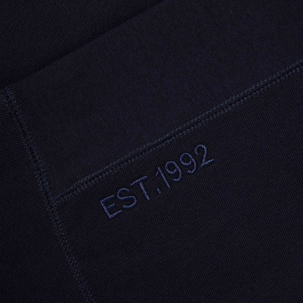 A close-up of the ‘EST. 1992’ embroidery on the Lanzera Club Crewneck in Navy Clásico. This tonal detail, subtly placed near the hem, celebrates Lanzera’s establishment and long-standing connection to the artistry of football.