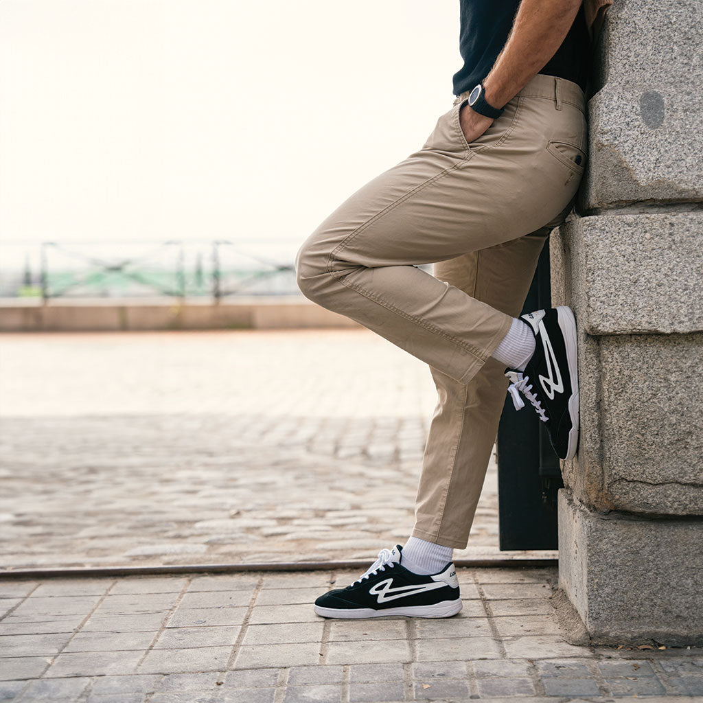 A person leaning against a stone wall wearing Lanzera Jackal black suede sneakers, showcasing their fusion of football heritage and modern streetwear style.