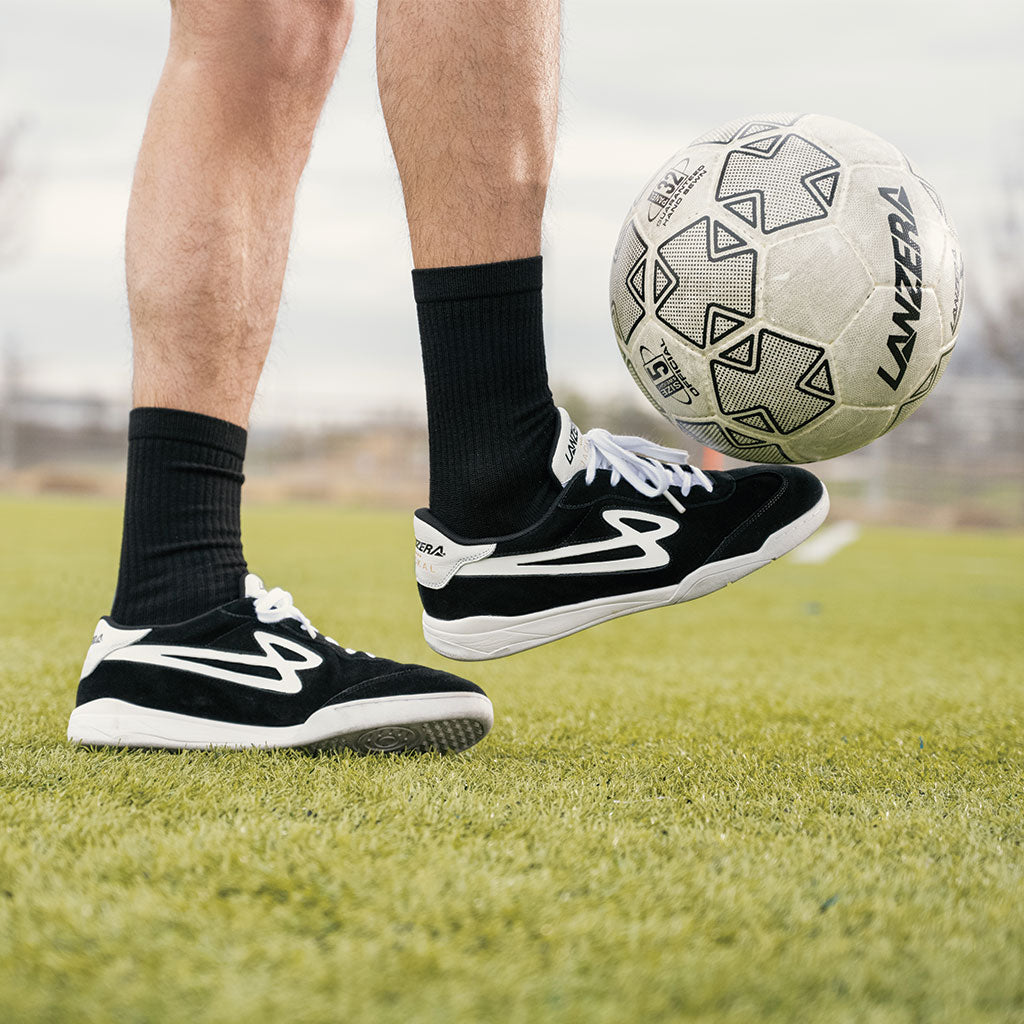 A player juggling a soccer ball while wearing Lanzera Jackal black suede sneakers, showcasing the responsive touch, durable non-marking sole, and hybrid futsal-street design.