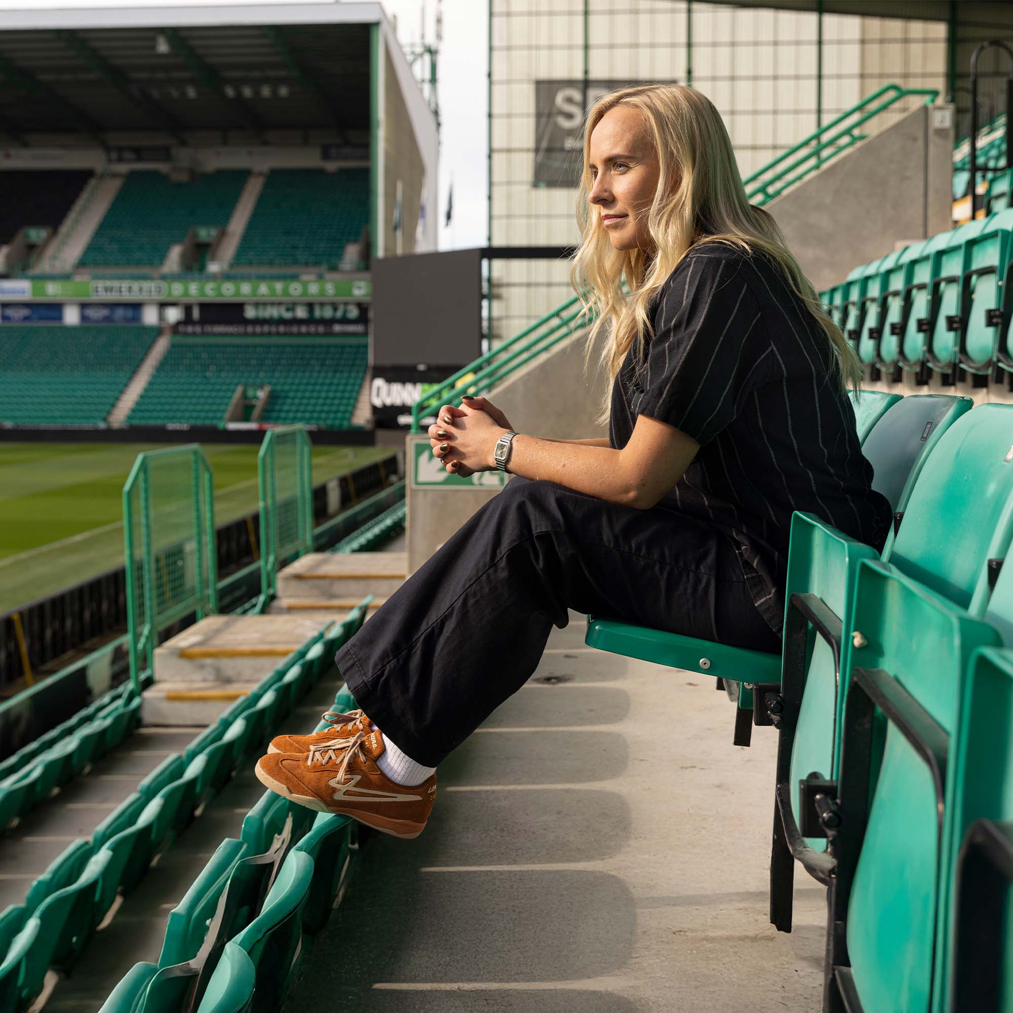 Person sitting on Easter Road stadium wearing Lanzera Jackal in caramello brown with a sports field in the background