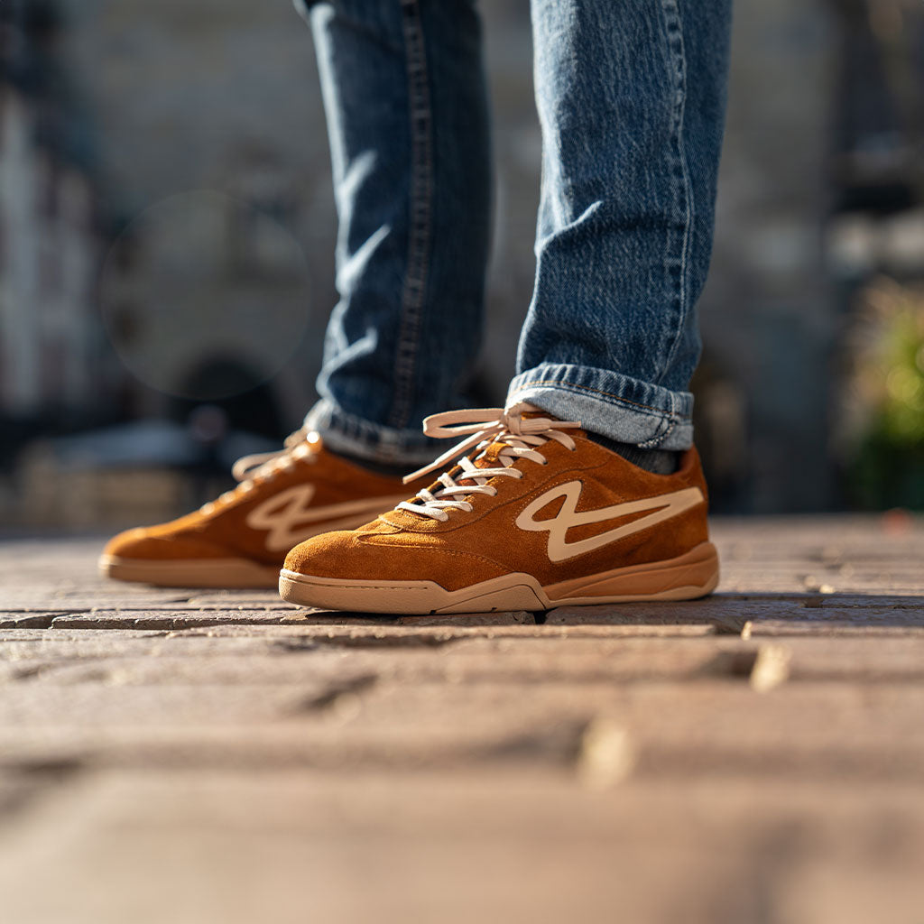 Lanzera Jackal Caramello suede sneakers worn with jeans on a cobblestone street, showcasing the blend of football heritage and casual street style.