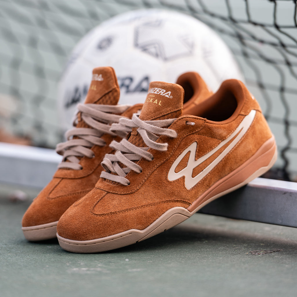 Lanzera Jackal Caramello suede sneakers resting on an outdoor futsal court, highlighting the rich suede upper, gum sole, and embossed branding for a classic football-inspired look.