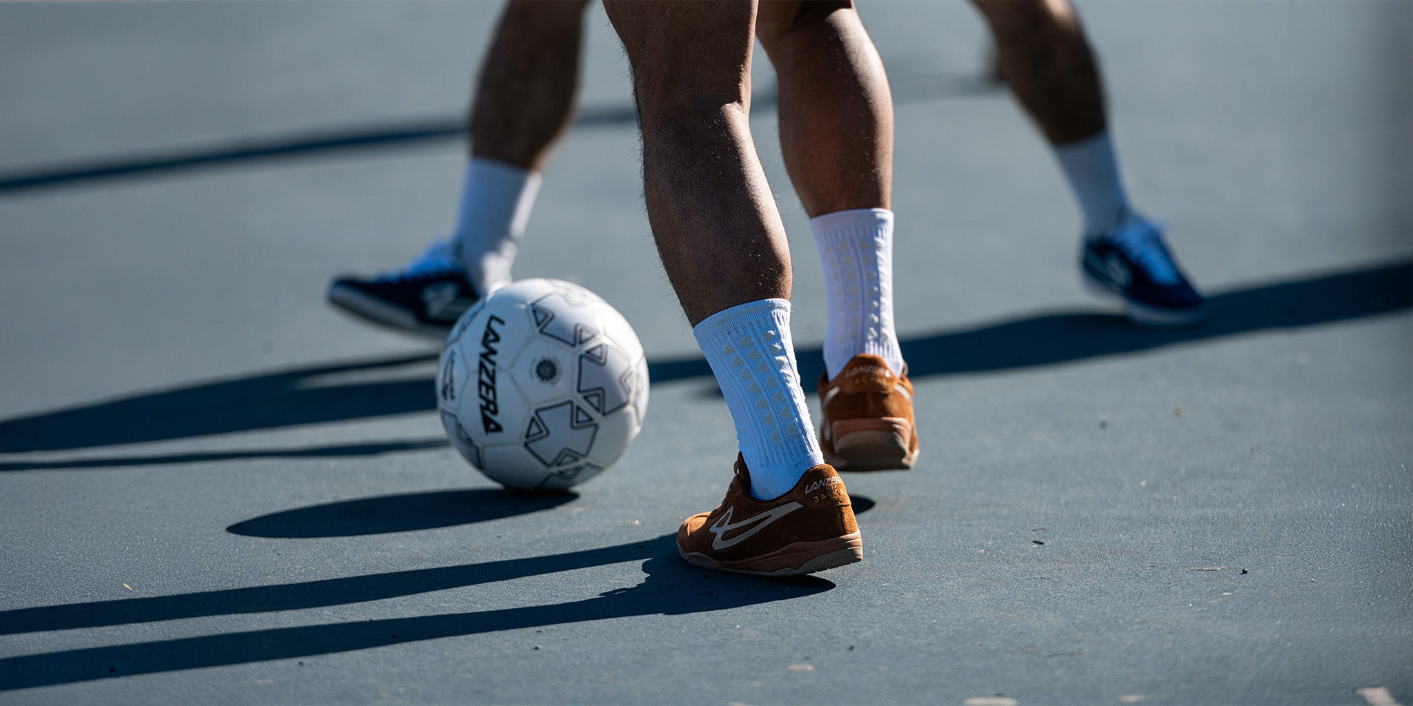 Close-up of players wearing Lanzera Jackal futsal shoes in Caramello and Navy during a street football game, highlighting the shoe’s suede texture and movement.