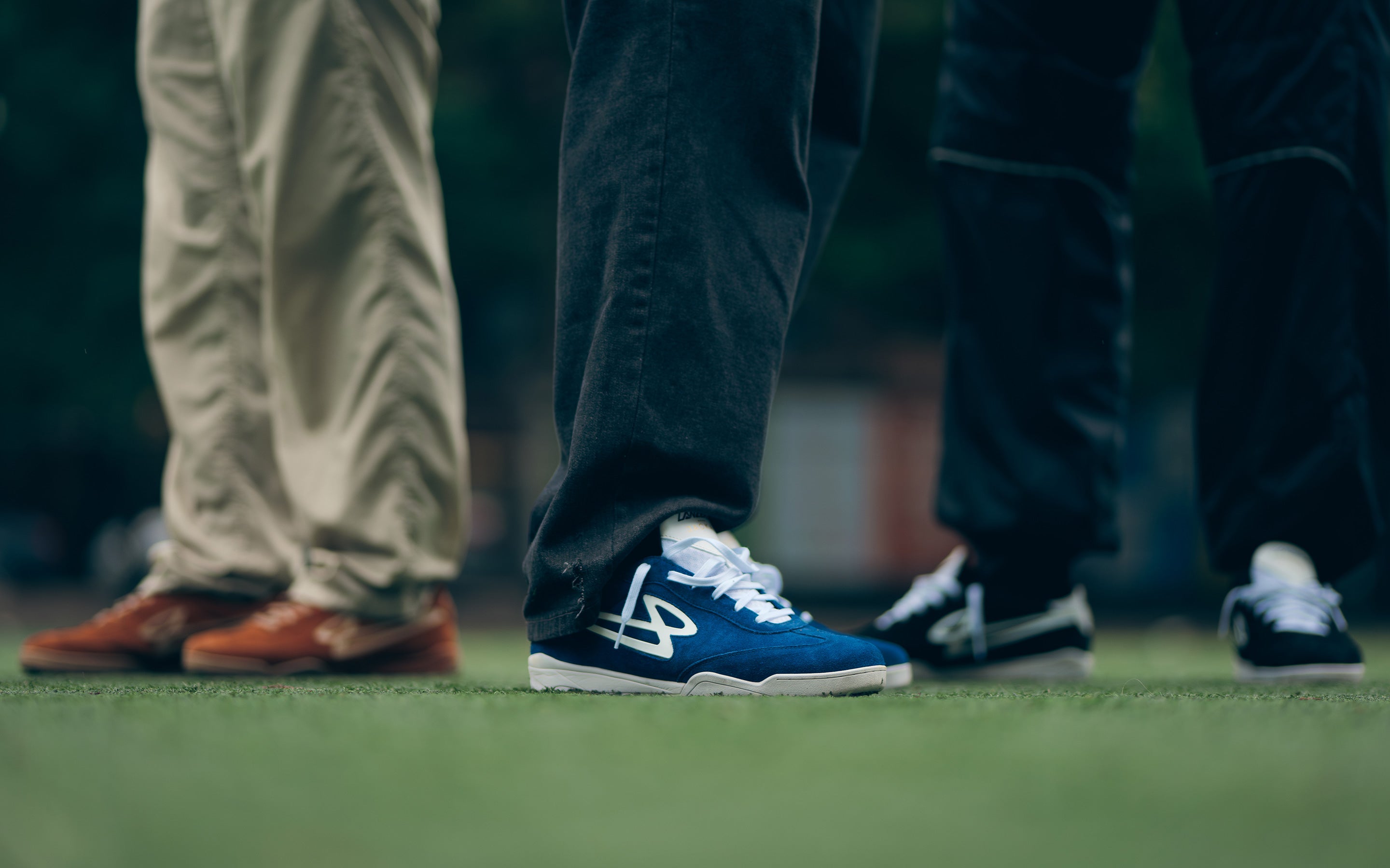 Close-up of three people wearing Lanzera Jackal suede leather shoes in navy, black, and caramello on a turf field, showcasing their fusion of football culture and modern streetwear style.