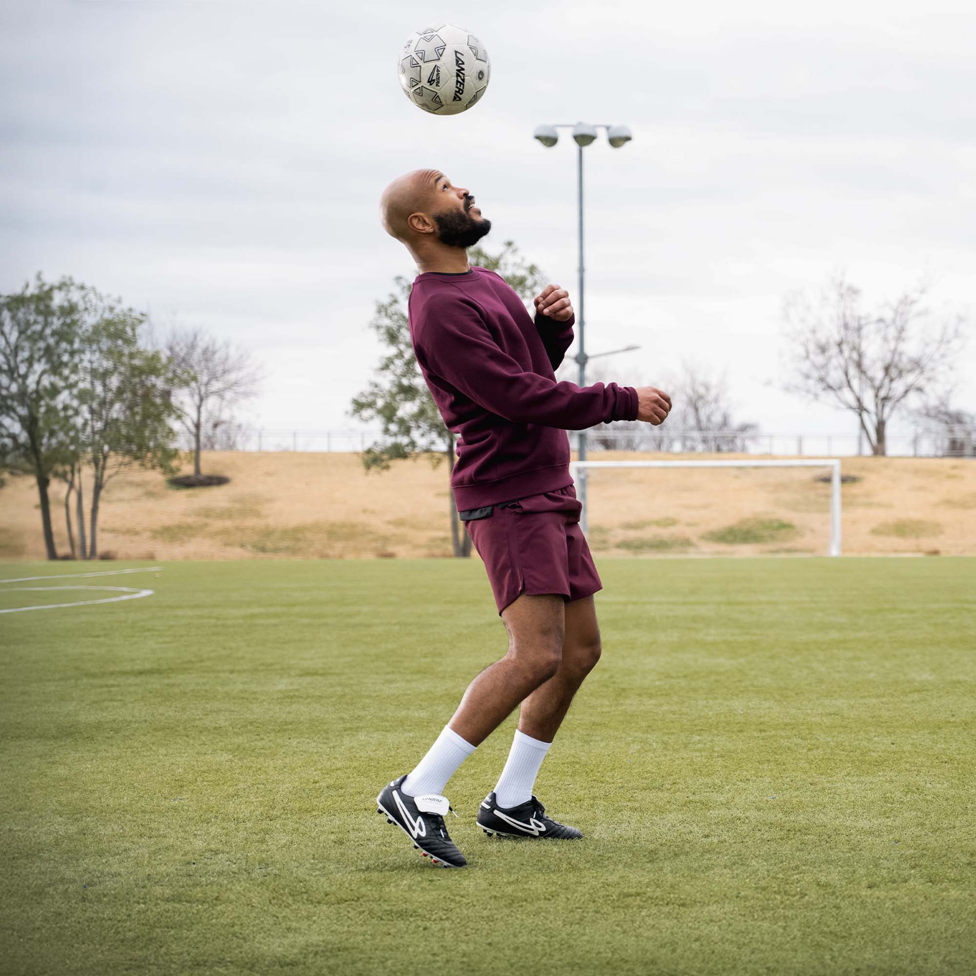 Player wearing Lanzera Professionale cleats, heading the ball on a natural grass pitch.