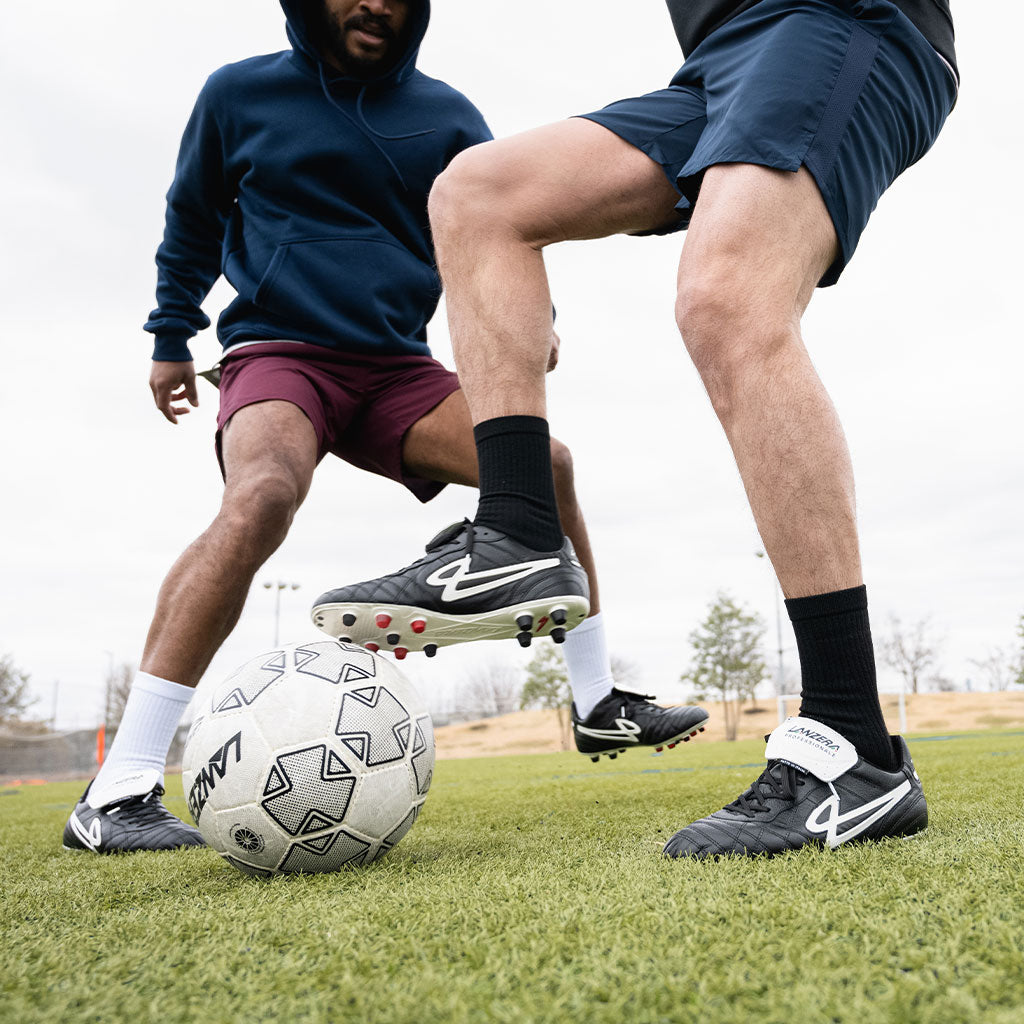 Two players wearing Lanzera Professionale soccer cleats battling for possession, showcasing the aggressive traction from the firm ground soleplate and the stability of the premium leather upper.