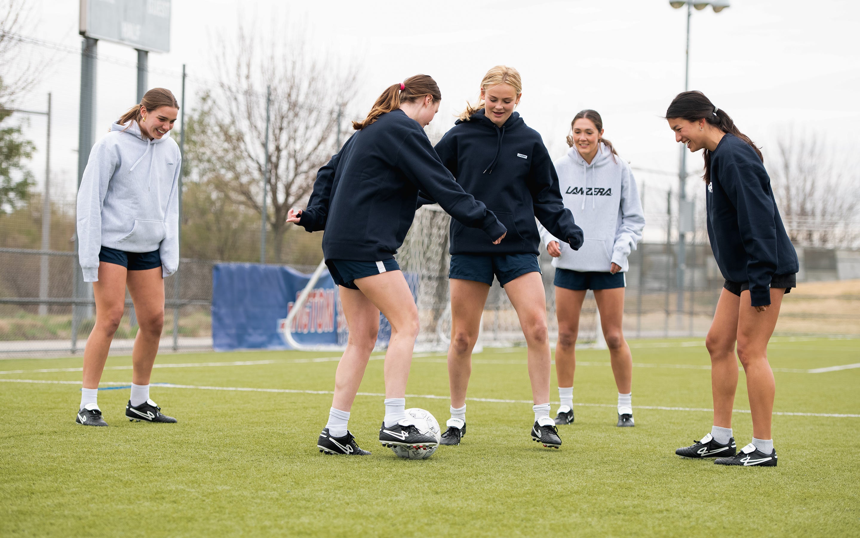 A group of female footballers playing rondo on the pitch, wearing Lanzera Professionale K-leather soccer cleats and Lanzera apparel. Designed for precision, ball control, and effortless movement, these cleats celebrate the artistry of the game.